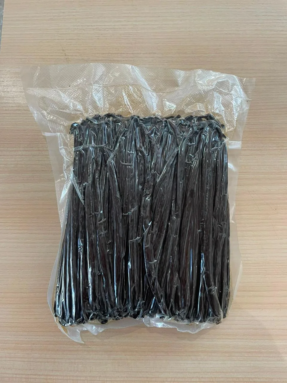 Vacuum-sealed bag of cured vanilla beans on a wooden table